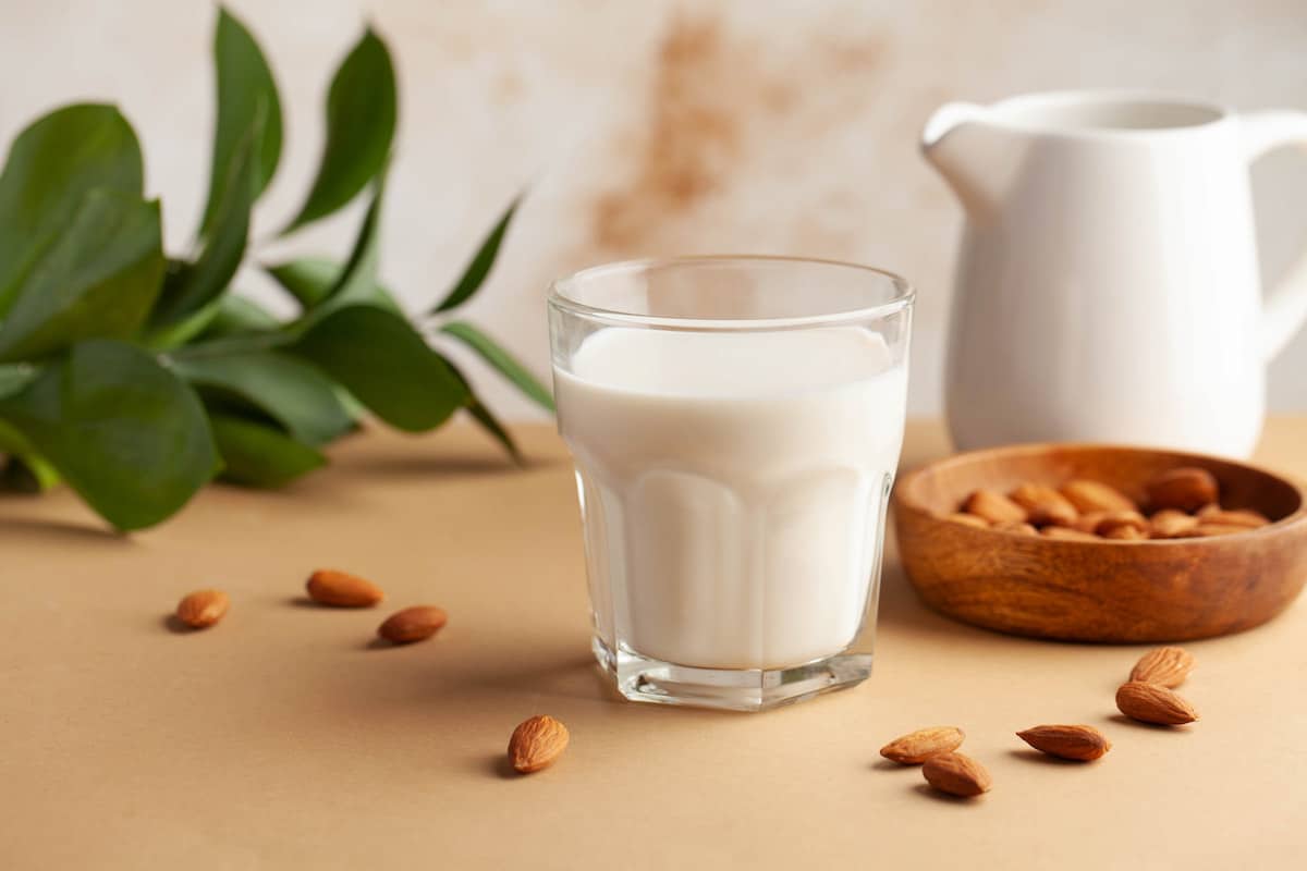 Glass of almond milk sitting on a table with almonds scattered around it