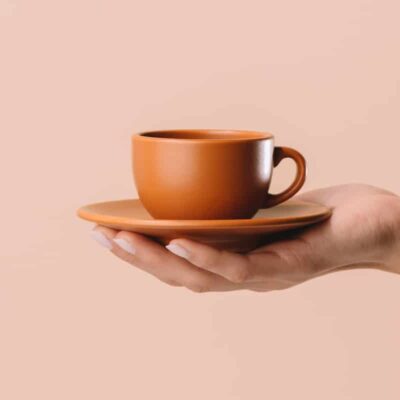 Hand holding an orange coffee mug against a beige background