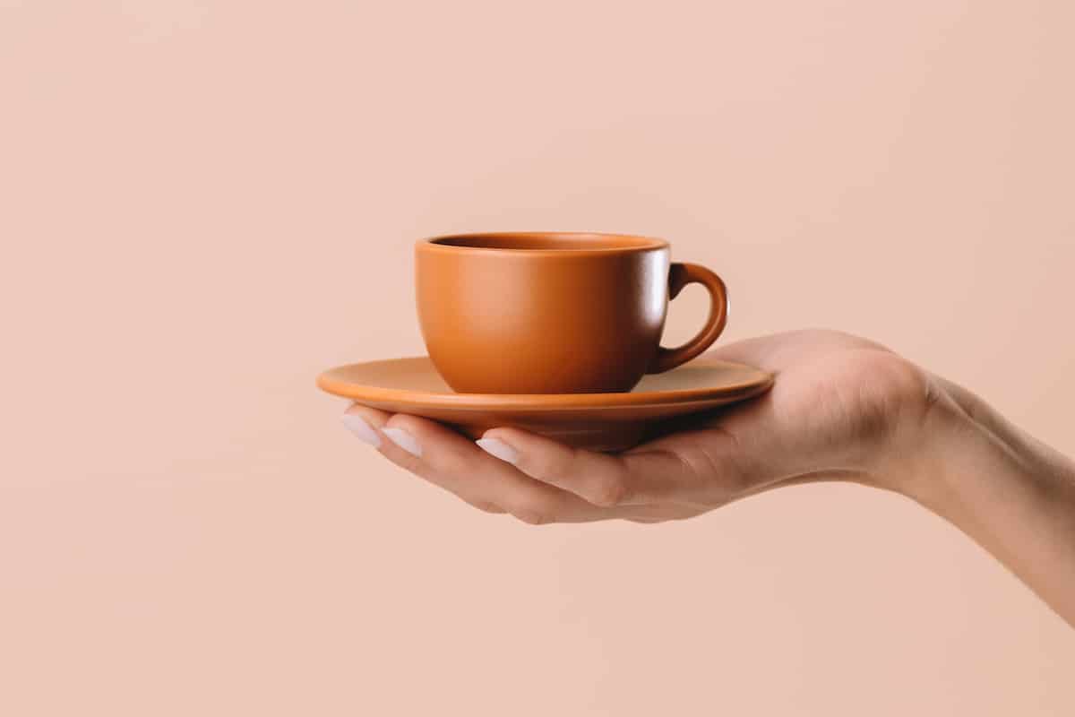 Hand holding an orange coffee mug against a beige background