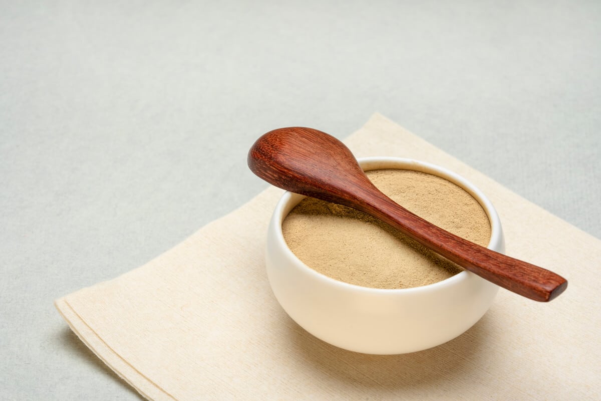 Ceramic bowl containing ashwagandha powder, with a wooden spoon on top
